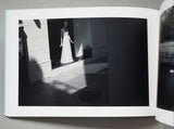 Open book showing a black and white photograph of a person in a white dress standing in a doorway.