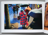 Open book showing a photograph of people with umbrellas on a rainy day.