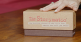 Storymatic product box on a wooden surface with a hand touching it