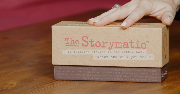 Storymatic product box on a wooden surface with a hand touching it